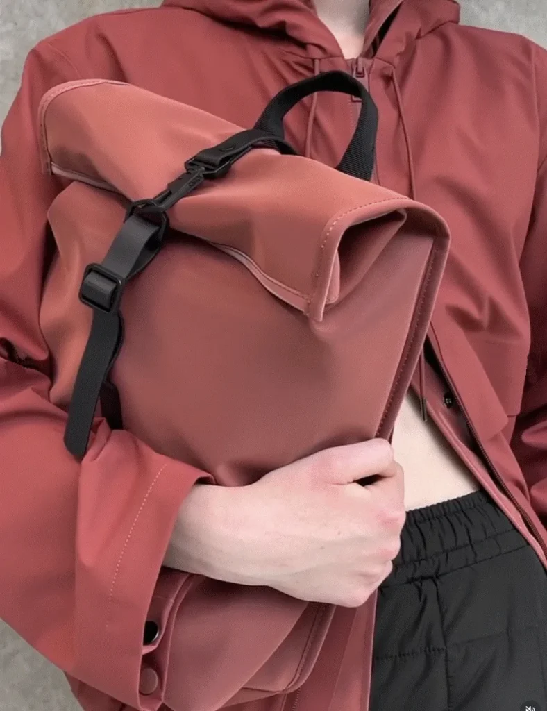 Model wearing a Rains waterproof jacket and carrying a Rolltop backpack